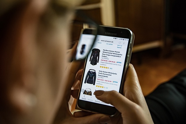 Ruce držící mobil Samsung s otevřeným nákupem zimních bund na Amazonu jako ilustrace online nakupování.