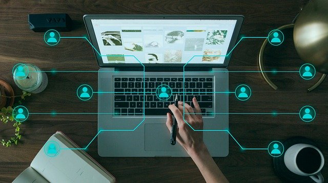 Notebook na dřevěném stole s ručně ovládaným kurzorem a propojenými ikonami uživatelů, ilustrace SEO trendů 2022.